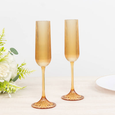 Two amber ribbed champagne flutes on a bright table setting