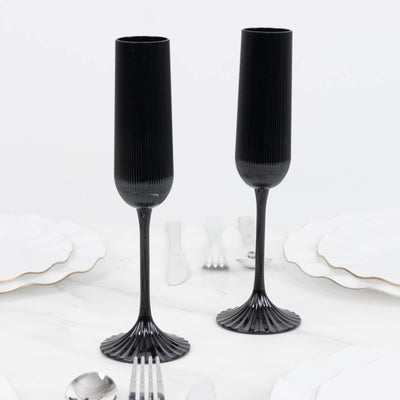 Black ribbed champagne flutes with fluted stems on a white table setting