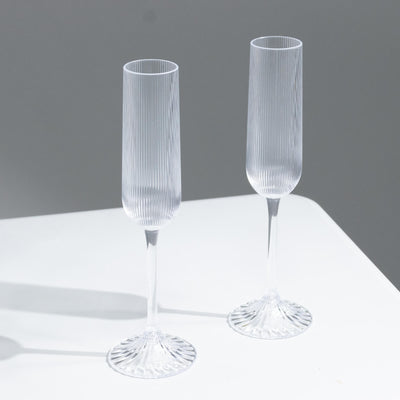 Two clear ribbed champagne flutes on a white table against a gray background