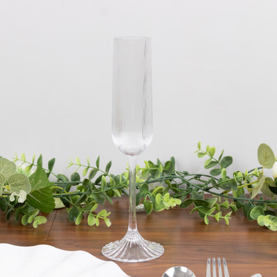 Clear ribbed champagne flute on wooden table with greenery decor