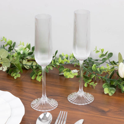 Clear ribbed champagne flutes on wooden table with greenery centerpiece