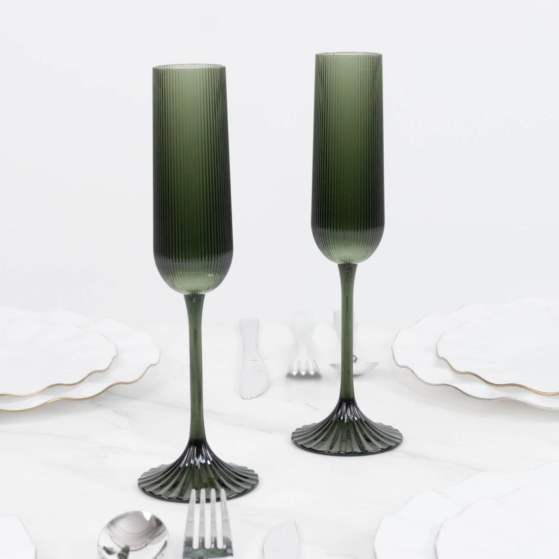 Green ribbed glass champagne flutes with fluted stems on a white marble table