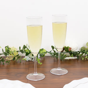 Two elegant champagne flutes filled with sparkling wine, surrounded by greenery.
