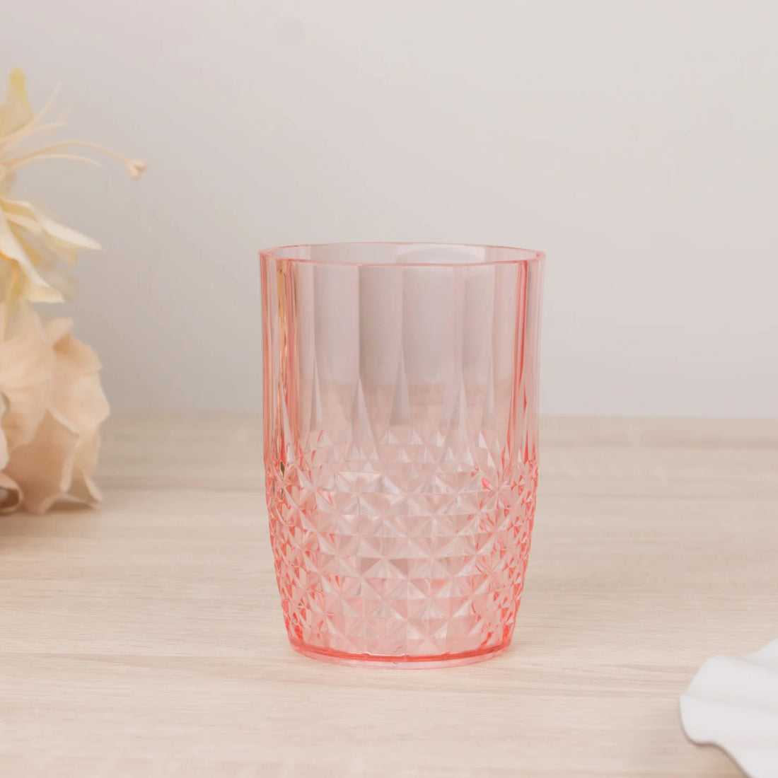 Pink crystal tumbler glass with a textured design on a wooden surface.