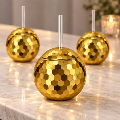 Gold disco ball cups with straws on a marble table for a 70s retro party