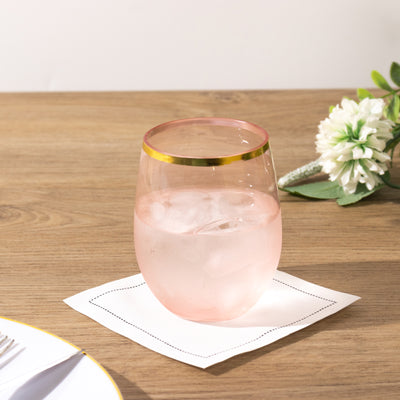 Pink glass with gold rim on a coaster, filled with ice water.