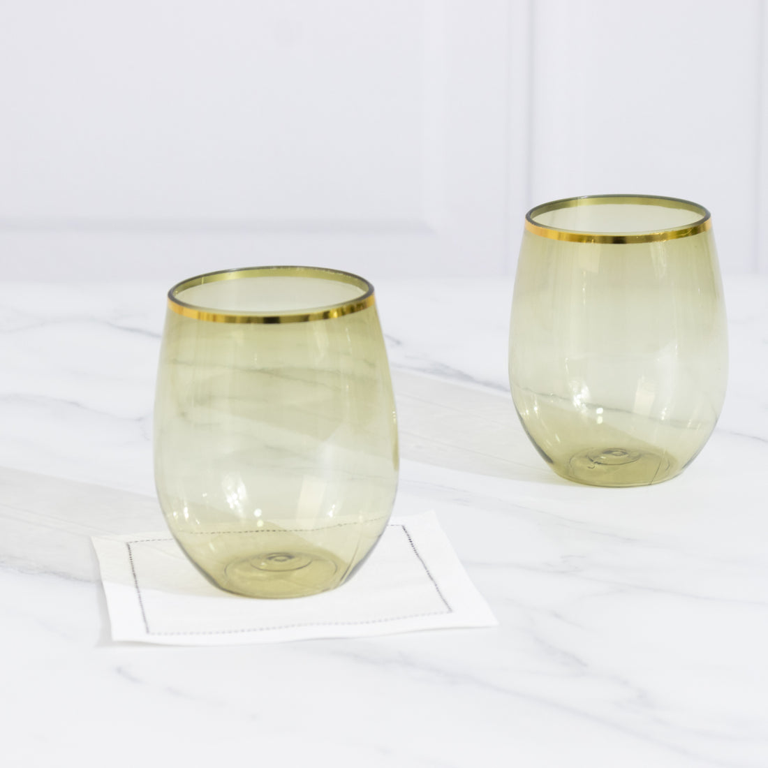 Set of two elegant green glasses with gold rims on a marble surface.