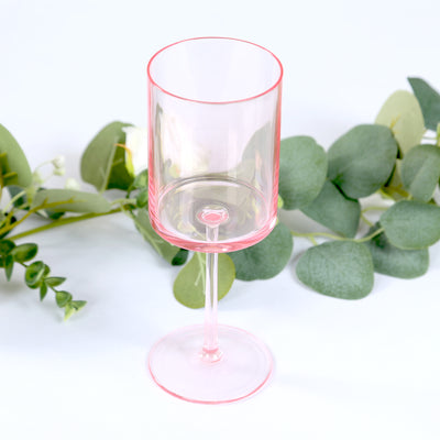 Pink transparent glass with a clear stem, surrounded by greenery.