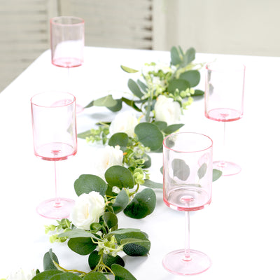 Pink stemmed glasses arranged with greenery and white flowers on a table.