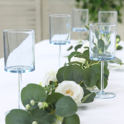 Blue stemmed glasses arranged on a table with greenery and flowers.