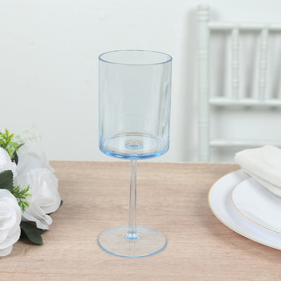 Blue stemmed glass on a wooden table with flowers and dinnerware.