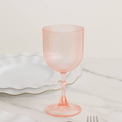 Pink ribbed glass goblet on marble table with white plate.