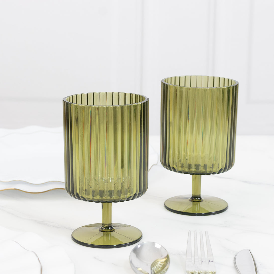 Green ribbed glass goblets on a marble table setting.