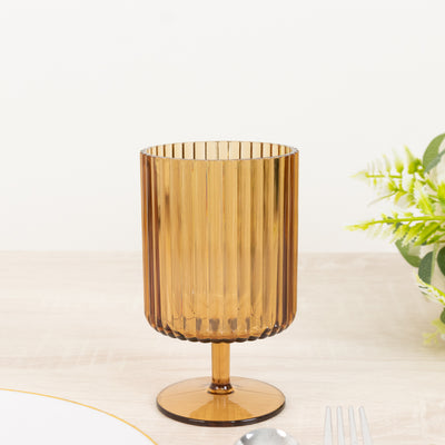 Amber ribbed glass cup on a table with cutlery and greenery.