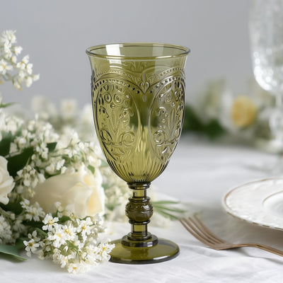 Green vintage glass goblet with intricate detailing, surrounded by flowers.