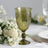 Green vintage glass goblet with intricate detailing, surrounded by flowers.