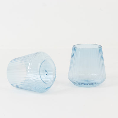 Blue ribbed glass tumblers on a plain background.