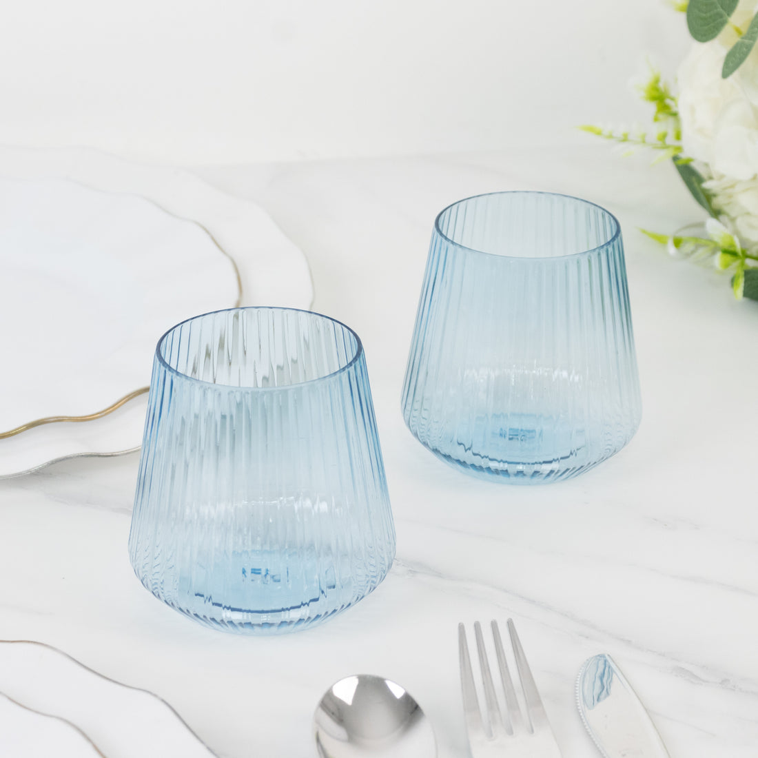 Set of two ribbed blue glass tumblers on marble surface.