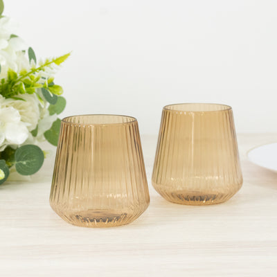 Two ribbed amber glasses on a light wooden surface with greenery.