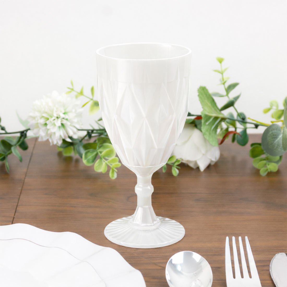 White textured plastic goblet on a wooden table with greenery