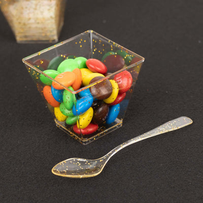 Colorful candy in a clear cup with a gold pattern and a plastic spoon.