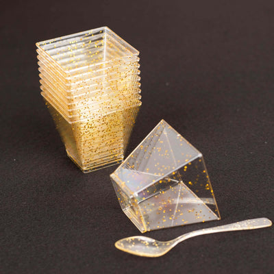 Clear plastic cups with gold glitter and a spoon, stacked and angled.