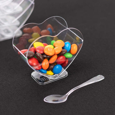 Clear heart-shaped candy cup with colorful chocolate candies and spoon.