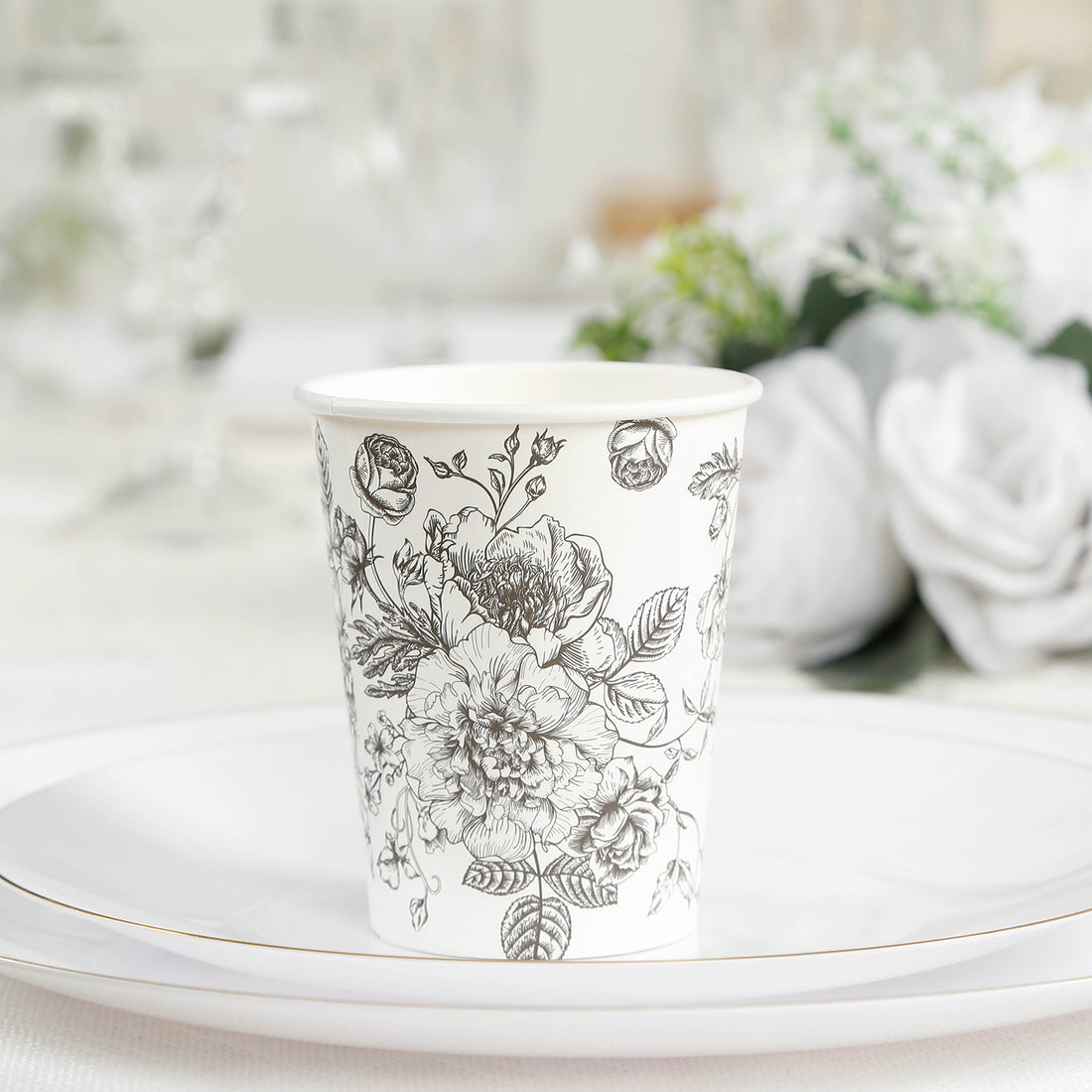 Floral design paper cup on a white plate with elegant table setting.