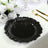 Black decorative plate with a ruffled edge on a dining table setting.