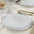 Elegant white dinner plates with intricate silver detailing on a festive table setting.