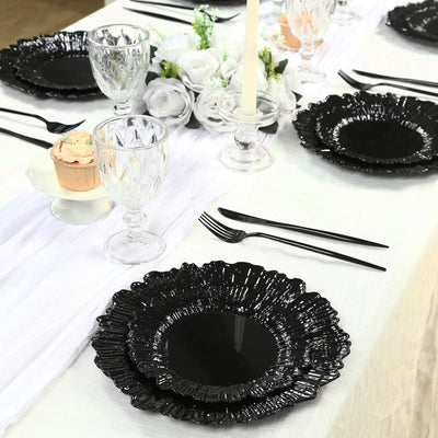 Black decorative plates set on a dining table with glassware and floral accents.