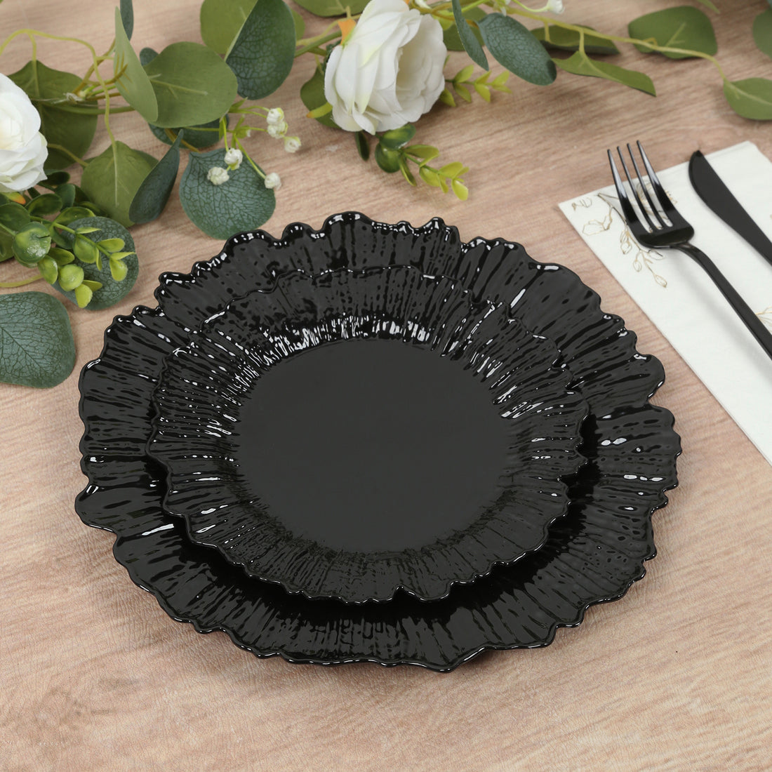 Black decorative plates with a floral edge design on a wooden table.