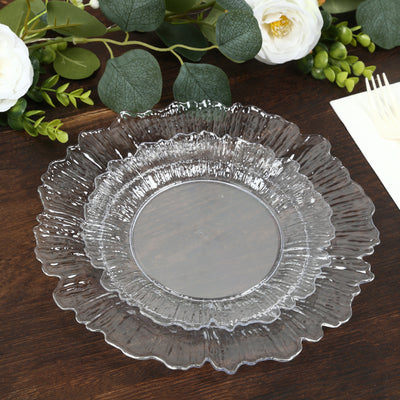 Clear decorative plates stacked on a wooden table with greenery and flowers.