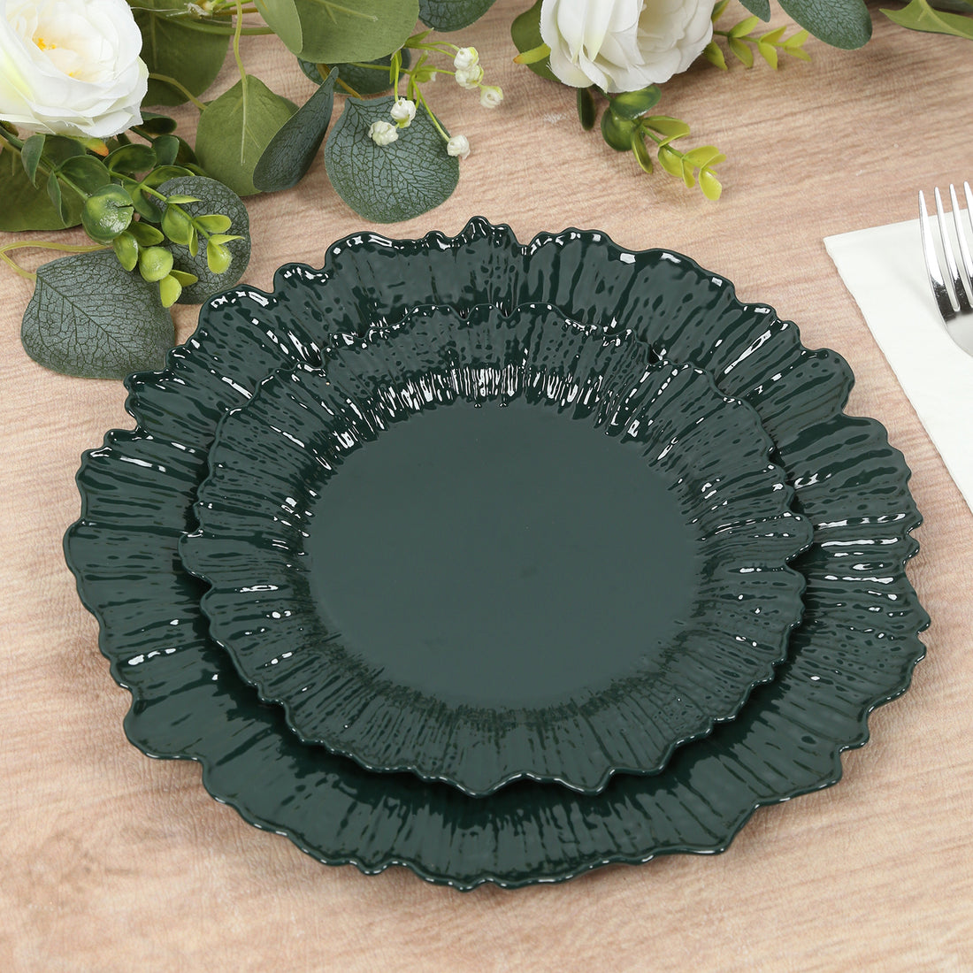 Dark green decorative plates stacked on a wooden table with greenery