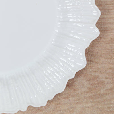 Textured white plate with a fluted edge on a wooden surface.