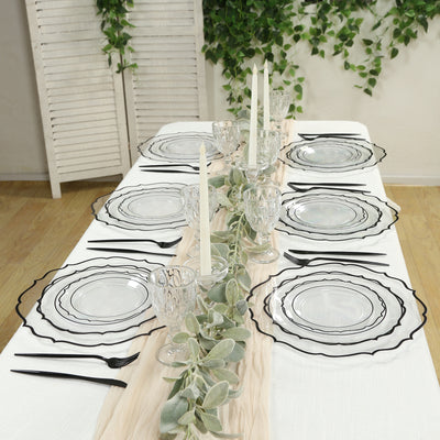 Elegant table setting with glassware, black-edged plates, and greenery accents.