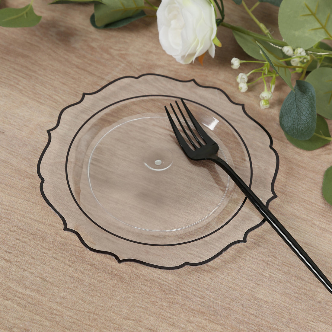 Clear decorative plate with black rim and fork on a wooden table.