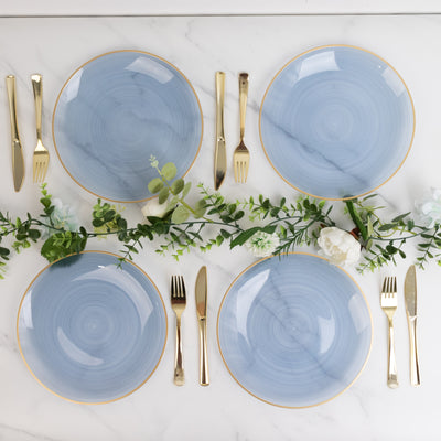 Set of four blue plates with gold rims arranged with cutlery and greenery.