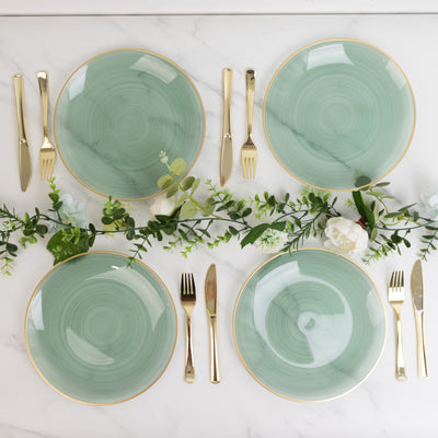 Elegant green plates with gold rims arranged with cutlery and greenery decor.