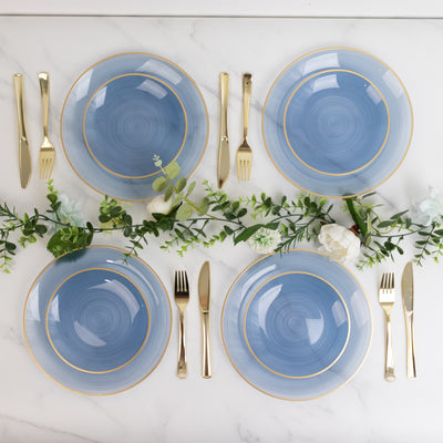 Blue dinner plates with gold rims arranged on a marble table with greenery.