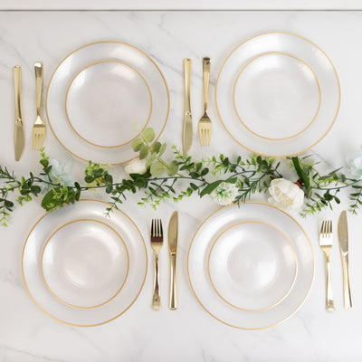 Elegant dinnerware set with gold trim, arranged on a marble table with greenery.