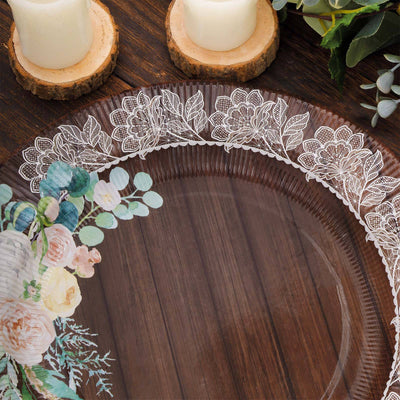 Clear decorative plate with floral design and lace trim on wooden table.