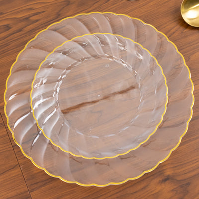 Clear plates with scalloped edges and gold trim on a wooden table.