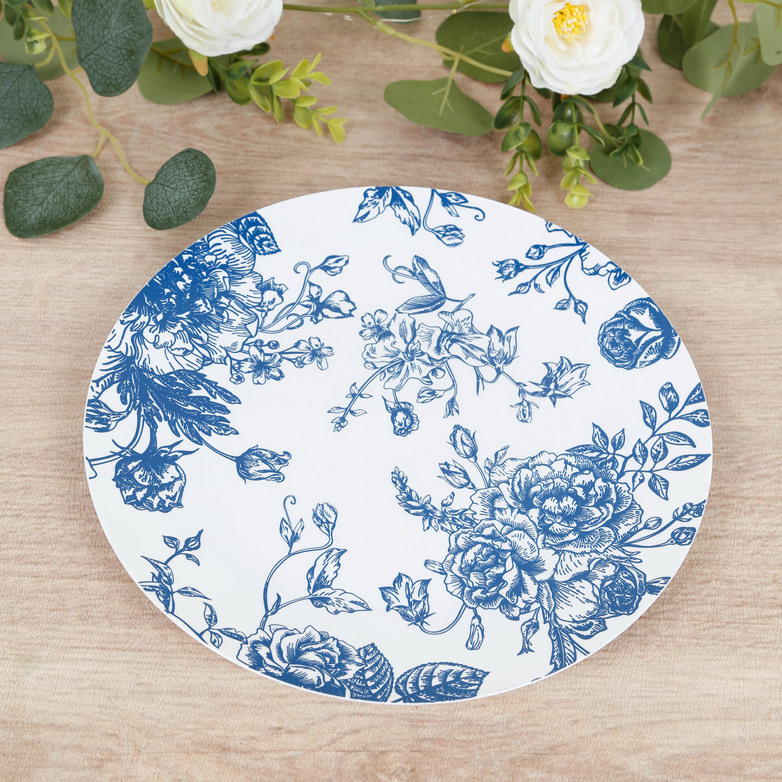 Blue floral decorative plate on a wooden surface with greenery.