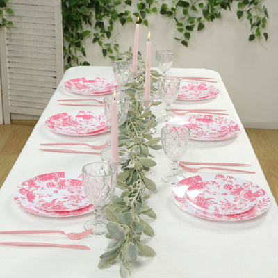 Pink floral dinnerware set arranged on a dining table with candles and greenery.