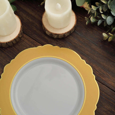 Elegant gold rimmed plate on wooden table with candles and greenery.