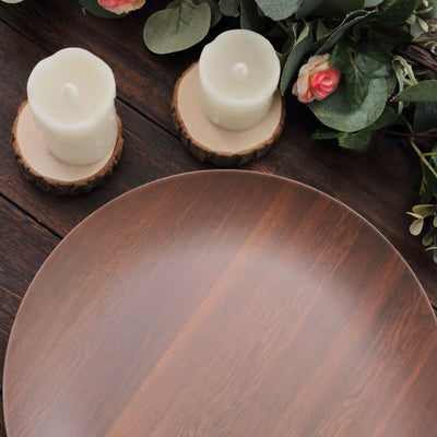 Wooden serving plate with candles and greenery on a rustic wooden table.
