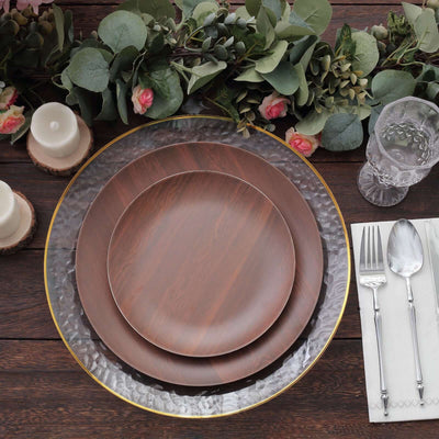 Elegant wooden dinner plates set on a rustic table with greenery and candles.