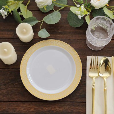 Elegant white plate with gold rim on a wooden table with greenery and candles.