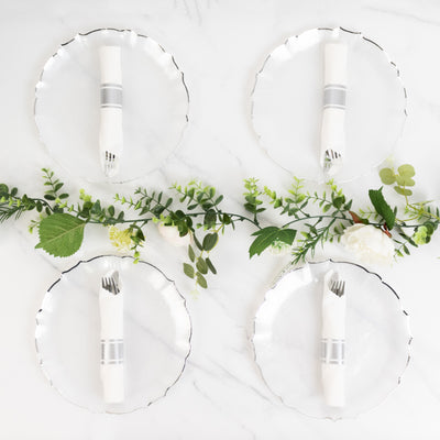 Elegant dining setup with clear plates and silverware, adorned with greenery.